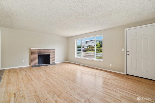 unfurnished living room with a textured ceiling, light hardwood / wood-style flooring, and a brick fireplace