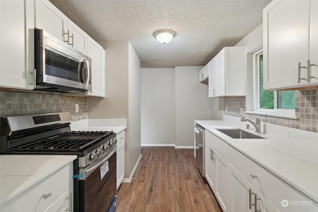 kitchen featuring stainless steel appliances, white cabinetry, sink, and light stone countertops