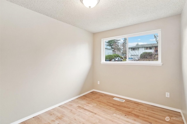 spare room with a textured ceiling and light hardwood / wood-style floors