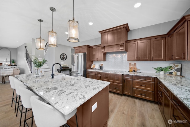 kitchen with high end refrigerator, tasteful backsplash, a kitchen island with sink, sink, and pendant lighting