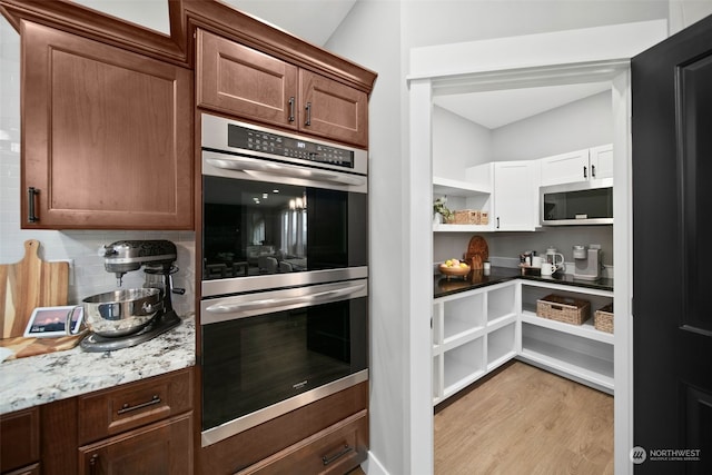 kitchen with light hardwood / wood-style flooring, appliances with stainless steel finishes, tasteful backsplash, light stone counters, and dark brown cabinetry