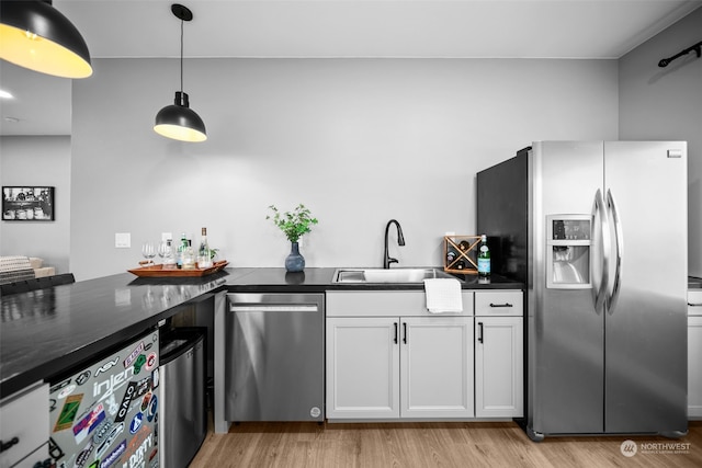 kitchen featuring light wood-type flooring, stainless steel appliances, sink, white cabinetry, and hanging light fixtures