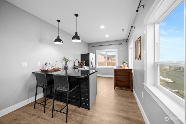 kitchen with a kitchen bar, stainless steel refrigerator with ice dispenser, kitchen peninsula, decorative light fixtures, and light hardwood / wood-style floors