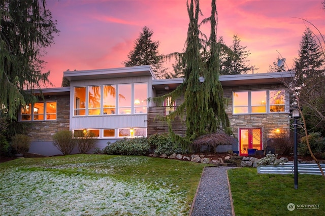 back house at dusk featuring a sunroom and a yard