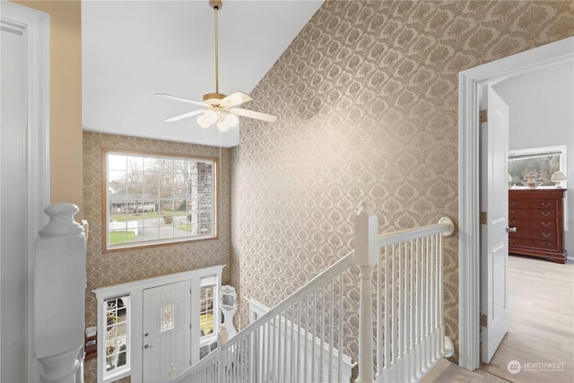 hall with wallpapered walls, wood finished floors, and an upstairs landing