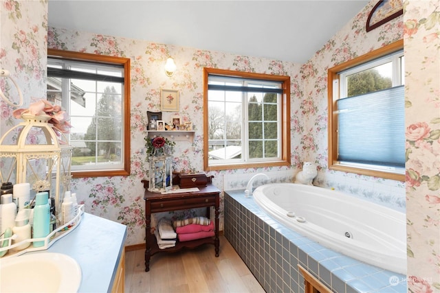 bathroom featuring a jetted tub, wallpapered walls, wood finished floors, and vanity