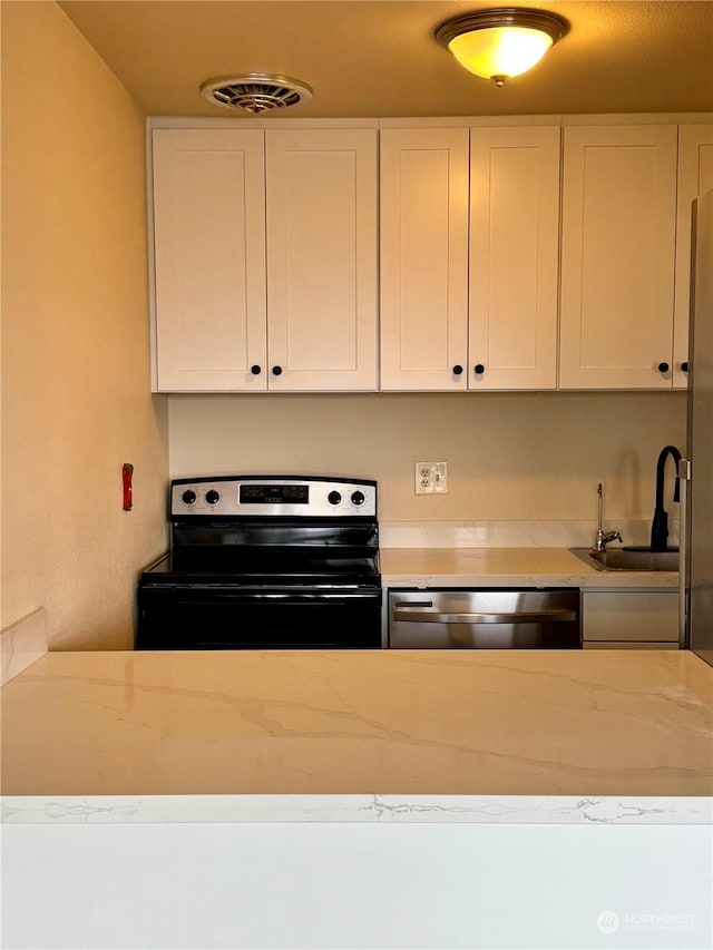 kitchen with light stone countertops, white cabinetry, sink, and stainless steel appliances