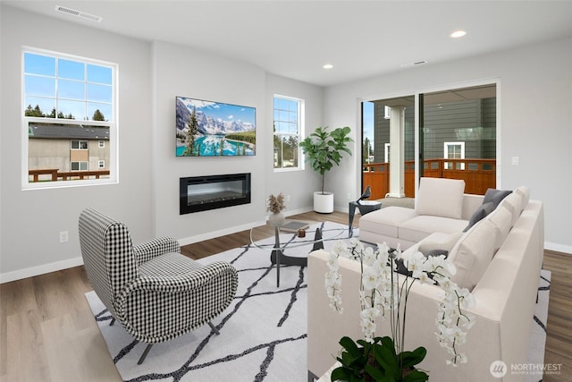 living room with visible vents, wood finished floors, a glass covered fireplace, recessed lighting, and baseboards