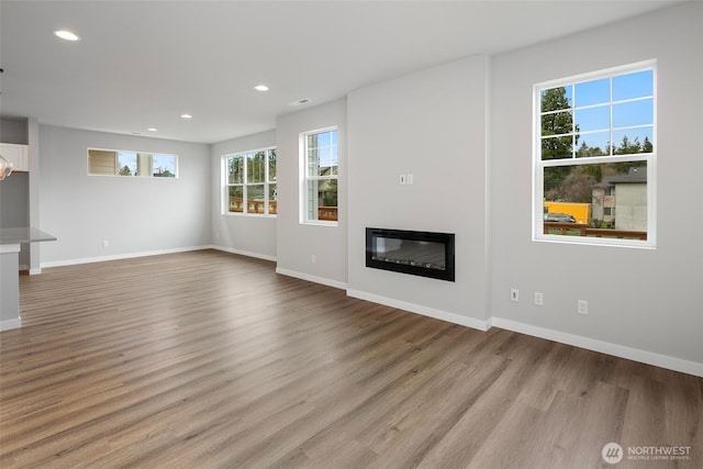 unfurnished living room featuring light wood-type flooring, baseboards, and a glass covered fireplace