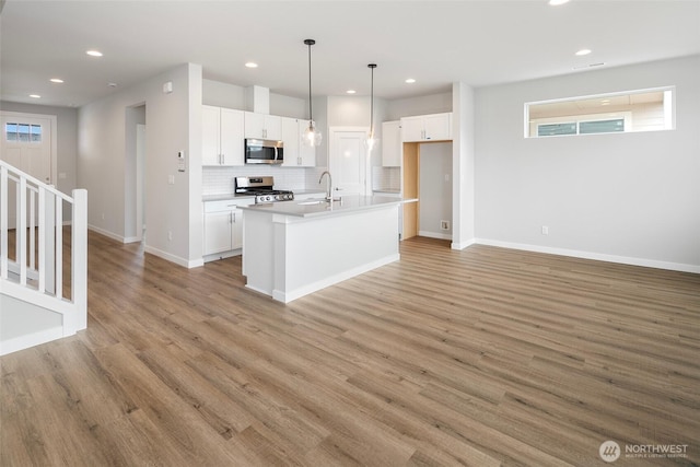 kitchen with tasteful backsplash, light wood-type flooring, appliances with stainless steel finishes, white cabinets, and a sink