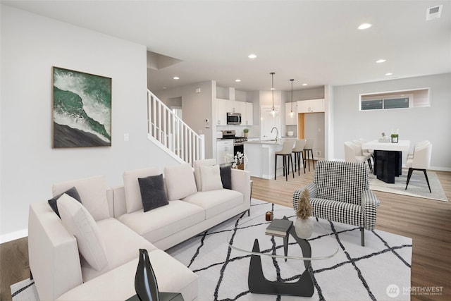 living area with light wood finished floors, visible vents, recessed lighting, and stairs