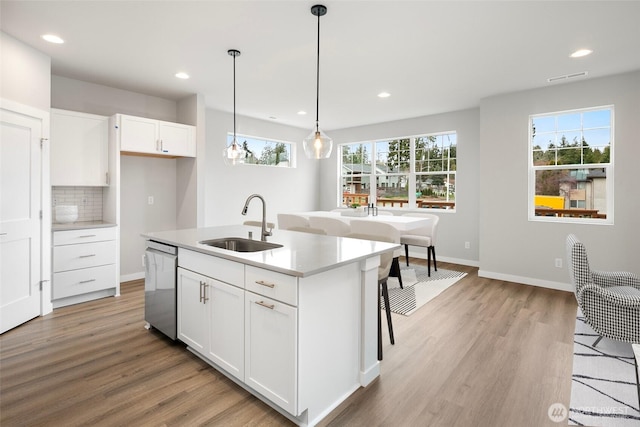 kitchen with visible vents, light wood-style flooring, a sink, decorative backsplash, and dishwasher