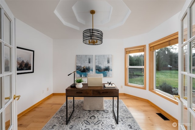 home office with a wealth of natural light, a tray ceiling, and light hardwood / wood-style flooring