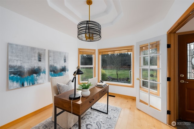 home office with light wood-type flooring and a raised ceiling