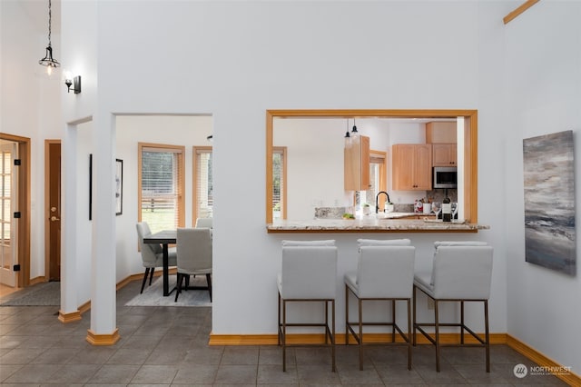 kitchen with kitchen peninsula, light brown cabinetry, hanging light fixtures, a high ceiling, and a breakfast bar