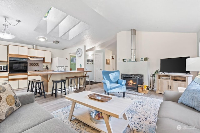 living room with sink, lofted ceiling with skylight, and light hardwood / wood-style flooring