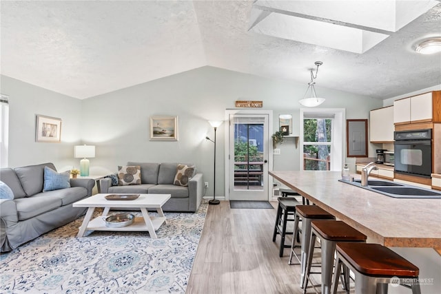 living room with sink, light wood-type flooring, vaulted ceiling, and a textured ceiling