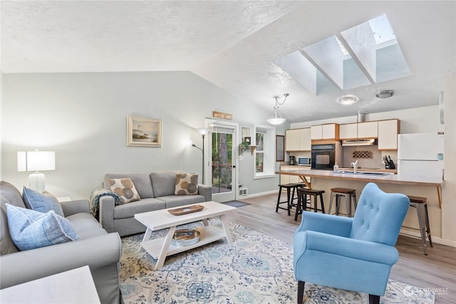 living room featuring a textured ceiling, light wood-type flooring, and vaulted ceiling with skylight