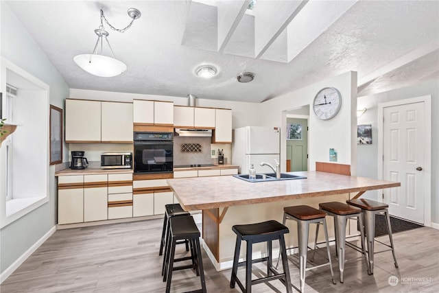 kitchen with black appliances, light hardwood / wood-style floors, a breakfast bar, sink, and decorative light fixtures