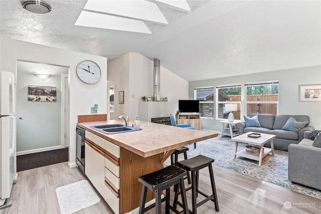 kitchen with sink, dishwasher, white fridge, light hardwood / wood-style flooring, and a center island with sink