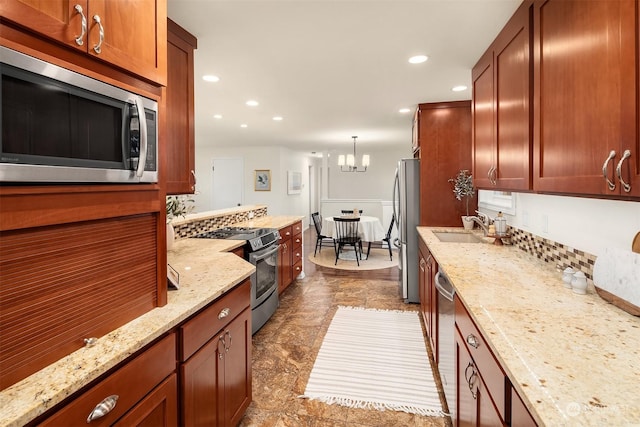 kitchen with a chandelier, stainless steel appliances, light stone countertops, sink, and decorative light fixtures