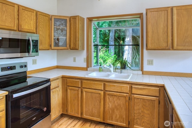 8917 SE Mcbreen Ln, Port Orchard, WA 98367 - kitchen featuring appliances with stainless steel finishes, tile counters, glass insert cabinets, and brown cabinets