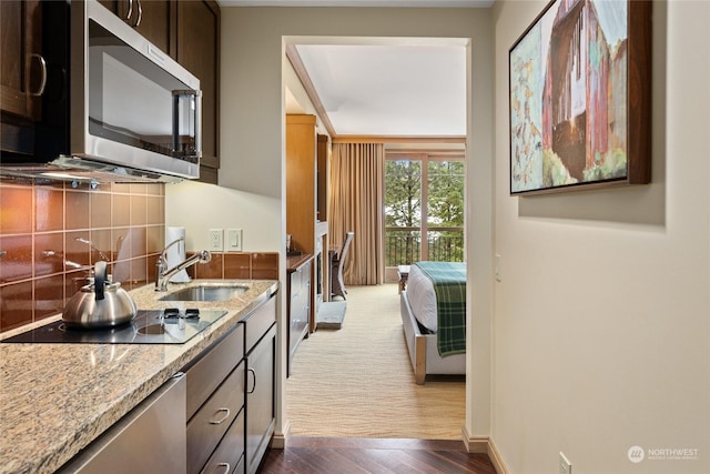 kitchen featuring backsplash, sink, light stone counters, dark hardwood / wood-style flooring, and dark brown cabinetry