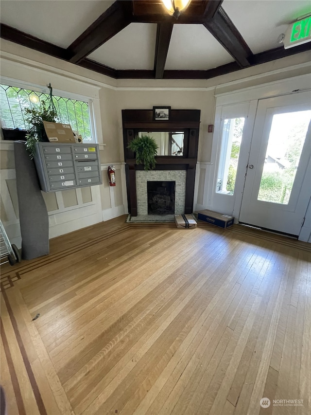 unfurnished living room with beam ceiling, coffered ceiling, a mail area, a fireplace, and light wood-type flooring