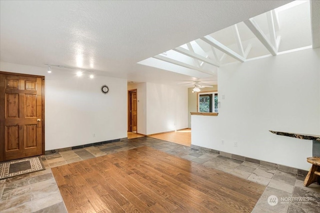 unfurnished living room with ceiling fan, rail lighting, a textured ceiling, and a skylight