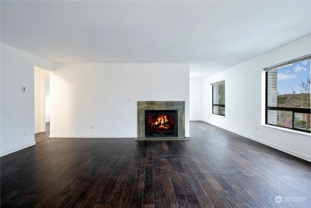 unfurnished living room featuring a fireplace with flush hearth, baseboards, and dark wood-type flooring