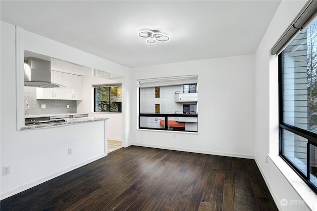 kitchen with dark wood-type flooring, white cabinetry, baseboards, backsplash, and wall chimney exhaust hood