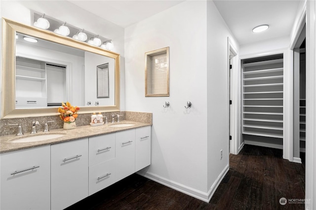 full bath with a spacious closet, wood finished floors, a sink, and baseboards