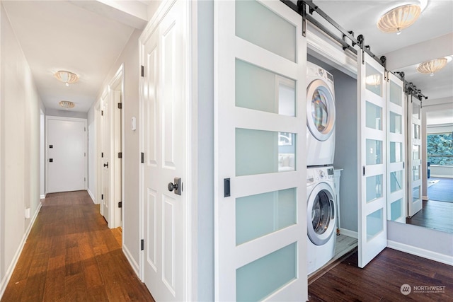 laundry area with dark wood-type flooring, laundry area, stacked washing maching and dryer, and a barn door