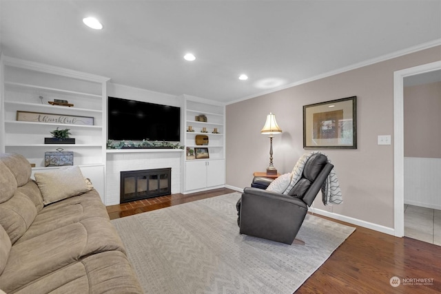 living room with a brick fireplace, dark wood-type flooring, built in shelves, and crown molding