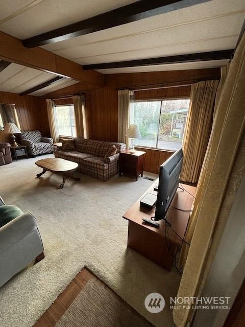 living room featuring light colored carpet, wooden walls, and lofted ceiling with beams