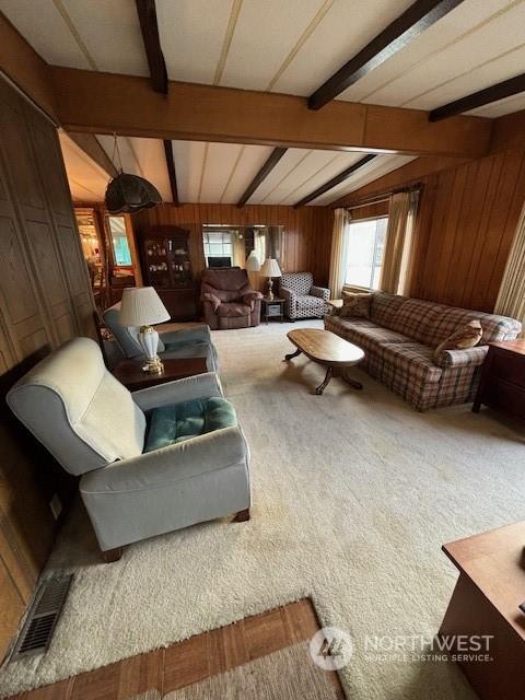 carpeted living room featuring wooden walls and lofted ceiling with beams