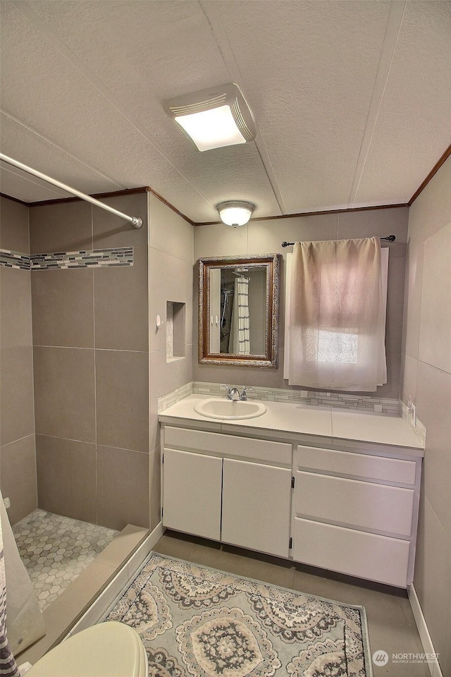 bathroom featuring a textured ceiling, tile patterned flooring, a tile shower, toilet, and vanity