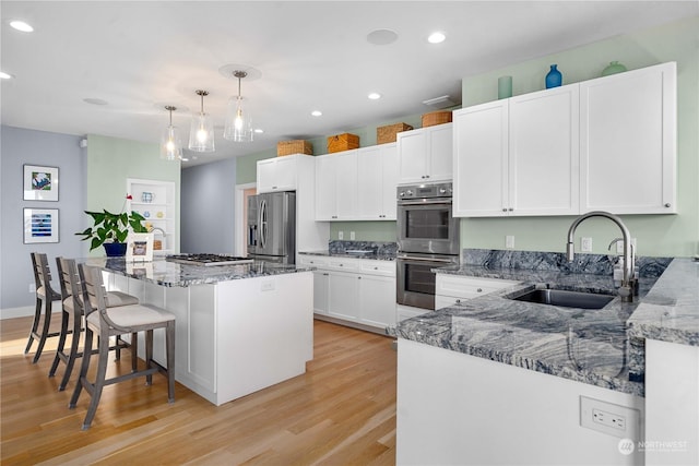 kitchen featuring pendant lighting, appliances with stainless steel finishes, a kitchen island, white cabinetry, and sink