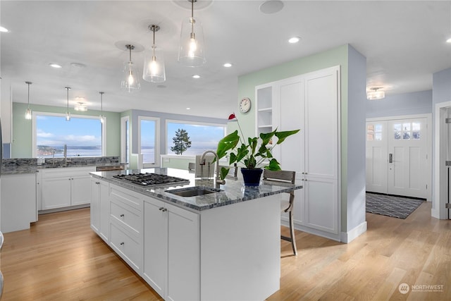 kitchen with hanging light fixtures, sink, white cabinetry, dark stone countertops, and a center island with sink