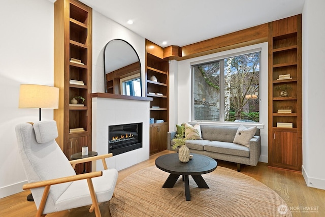 living area with recessed lighting, baseboards, built in features, light wood finished floors, and a glass covered fireplace