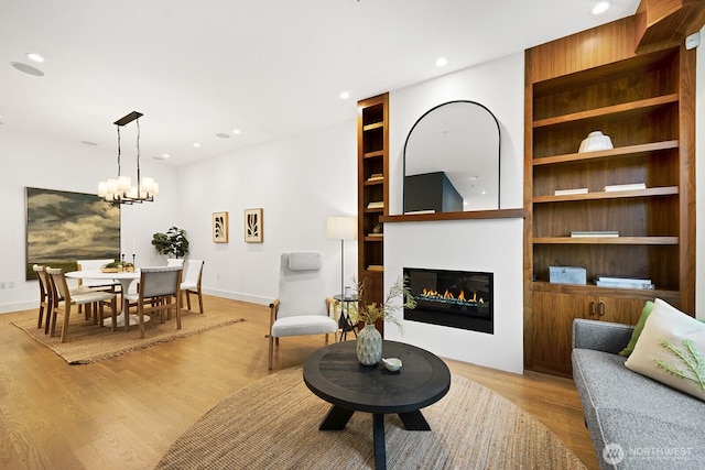 living area featuring recessed lighting, baseboards, built in features, light wood finished floors, and a glass covered fireplace