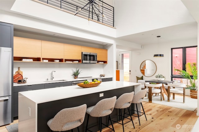 kitchen featuring appliances with stainless steel finishes, hanging light fixtures, light wood-type flooring, a kitchen island, and sink