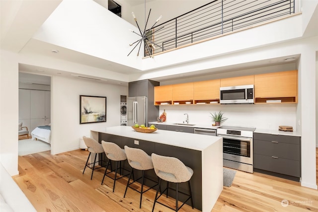 kitchen featuring a high ceiling, a breakfast bar, a kitchen island, appliances with stainless steel finishes, and stacked washer and clothes dryer