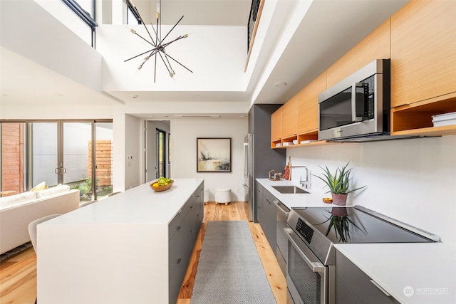 kitchen featuring stainless steel appliances, sink, a center island, an inviting chandelier, and light hardwood / wood-style flooring