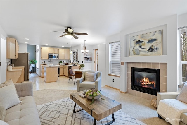 living room featuring ceiling fan with notable chandelier, a fireplace, sink, and a wealth of natural light