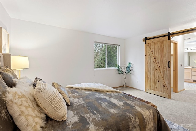 bedroom with ensuite bathroom, light colored carpet, and a barn door