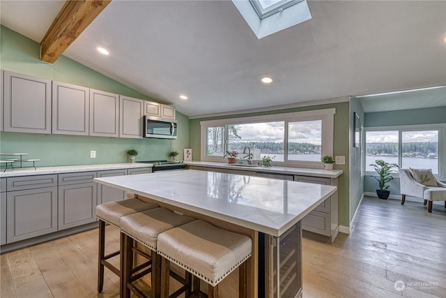 kitchen featuring appliances with stainless steel finishes, gray cabinets, a kitchen island, and vaulted ceiling with skylight