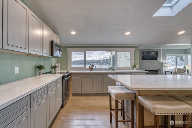 kitchen with light stone counters, a breakfast bar, a skylight, appliances with stainless steel finishes, and sink