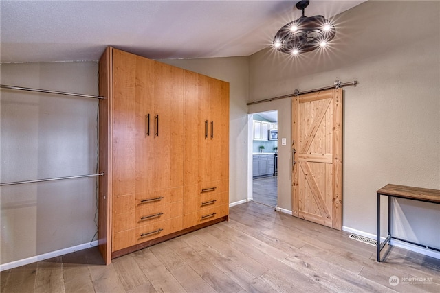 unfurnished bedroom featuring light hardwood / wood-style floors, vaulted ceiling, and a barn door