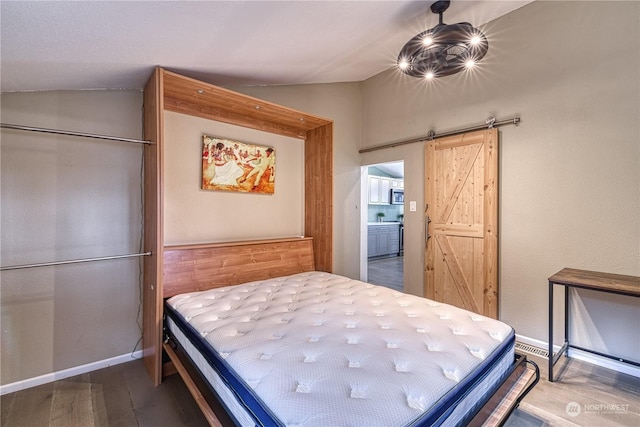 bedroom with lofted ceiling, wood-type flooring, and a barn door